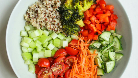 So funktioniert die DASH-Diät Schale mit verschiedenen geschnittenen und zubereiteten Gemüsesorten und Quinoa, darunter Brokkoli, rote Paprika, Gurke, Karotten, Kirschtomaten und Sellerie.