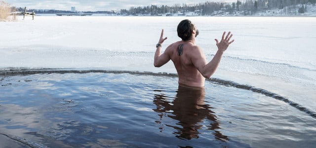 Urlaubstrend Retreat: So findest du die passende Auszeit (Foto: CC0 Public Domain / Unsplash.com – Mika Ruusunen) Ein Mann steht bis zur Taille in einem kreisrunden Loch im zugefrorenen See, umgeben von Eis und Schnee.