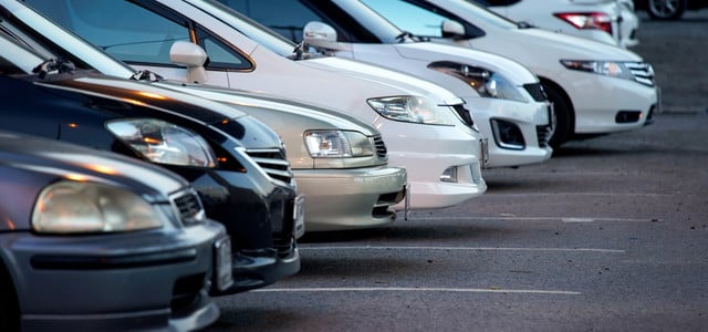 Reihe von geparkten Autos, hauptsächlich in Weiß und Schwarz, auf einem asphaltierten Parkplatz, Frontansicht der Fahrzeuge sichtbar.