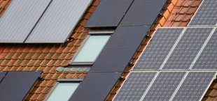 Dach mit roten Ziegeln, auf dem mehrere Solarpaneele und zwei Dachfenster installiert sind.