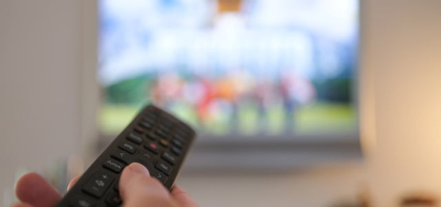 Eine Hand bedient eine Fernbedienung für ein TV-Gerät.