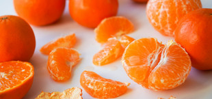 Mehrere Mandarinen, einige ganz, andere geschält, sowie einzelne Mandarinenstücke und Schalenstücke auf weißem Untergrund.