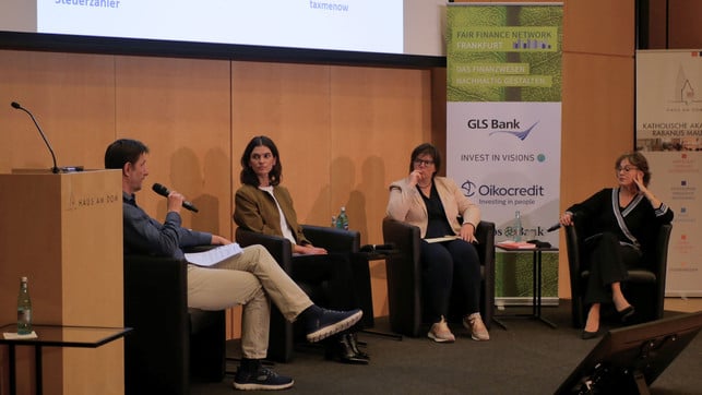 FairFinanceWeek_4_1920x1080px Vier Personen sitzen auf Sesseln auf einer Bühne und führen eine Podiumsdiskussion. Drei Frauen und ein Mann, der links mit einem Mikrofon spricht. Im Hintergrund sind Banner mit Logos von Fair Finance Network Frankfurt, GLS Bank und Oikocredit zu sehen. Die Umgebung wirkt professionell und formal.