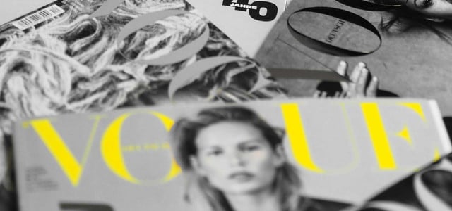 Mehrere Vogue-Magazine liegen auf einem Haufen, das Foto ist schwarz-weiß, bis auf einen gelben Vogue-Schriftzug.