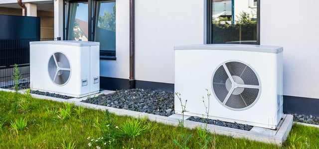 Zwei weiße Wärmepumpen stehen auf Betonplatten vor einem modernen Haus mit weißen Wänden und schwarzen Fensterrahmen.