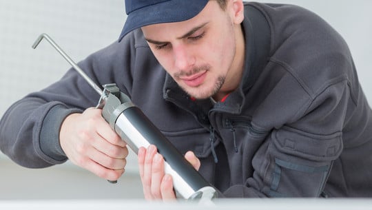 focused young technician sealing sink in clients kitchen Silikonfugen erneuern