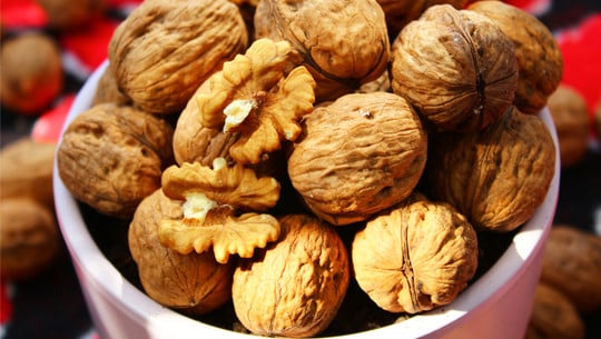 Gesunde Lebensmittel, die mehr Kalorien haben als Schokolade Eine weiße Schale gefüllt mit ganzen Walnüssen in der Schale und zwei aufgebrochenen Walnusshälften, die das Innere zeigen.