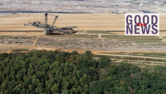 Hambi bleibt: Endlich steht fest, was mit dem Hambacher Forst passieren soll Großer Tagebau mit einer riesigen Abbau-Maschine in der Mitte, davor ein Waldgebiet, darüber der Schriftzug „GOOD NEWS“ in lila mit roten Pfeilen.