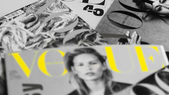 Erfolg für Tierschützer:innen: Vogue nimmt wichtige Änderung vor Mehrere Vogue-Magazine liegen auf einem Haufen, das Foto ist schwarz-weiß, bis auf einen gelben Vogue-Schriftzug.