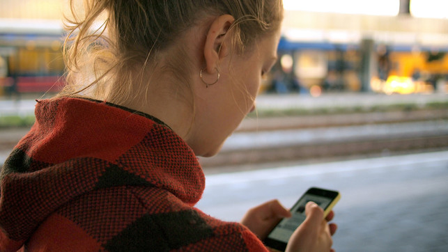 Eine Frau bedient ihr Smartphone. Sie steht an einem Bahnsteig. Lohnen sich smarte Thermostate