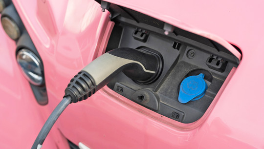 Hoher Verbrauch von Plug-In-Hybrid-Fahrzeugen Ladestecker eines pinkfarbenen Elektroautos, der in die Ladebuchse eingesteckt ist, daneben ein blauer Verschlussdeckel.