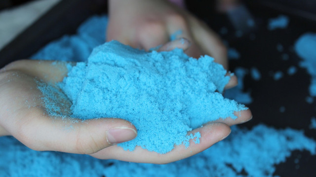 Eine Hand hält blauen Knetsand. Zwei Hände halten blauen Knetsand.
