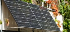 251020-speicher-balkonkraftwerk-sinnvoll-c Zwei Solarpaneele sind an ein Balkongeländer montiert, umgeben von grünen und herbstlich gefärbten Pflanzen.
