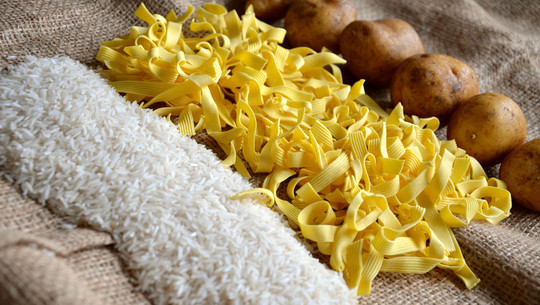 Reis, Nudeln oder Kartoffeln am gesündesten? Die Antwort ist eindeutig Weißer Reis, gelbe Bandnudeln und braune Kartoffeln liegen auf einem groben Jutesack.