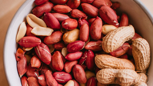 Jeden Tag Erdnüsse: Das sind die Folgen Schale mit Erdnüssen, teils mit roter Schale, teils geschält, sowie einige Erdnüsse in ihrer braunen Schale.