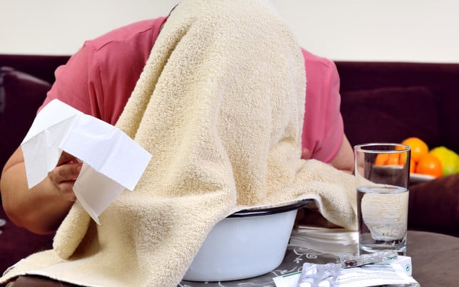 Ill women inhaling under a towel Ein wirksames Hausmittel gegen Heuschnupfen ist ein Dampfbad mit ätherischen Ölen.