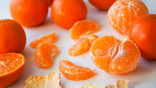 Jeden Tag Mandarinen essen? Mehrere Mandarinen, einige ganz, andere geschält, sowie einzelne Mandarinenstücke und Schalenstücke auf weißem Untergrund.