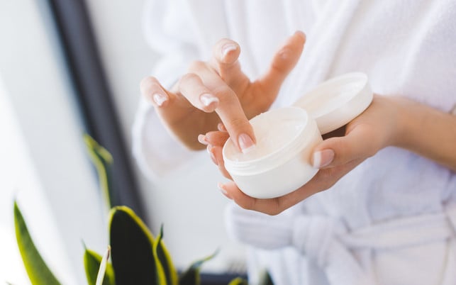 partial view of woman holding face cream in hands Massiere die Rosskastaniensalbe sanft ein.