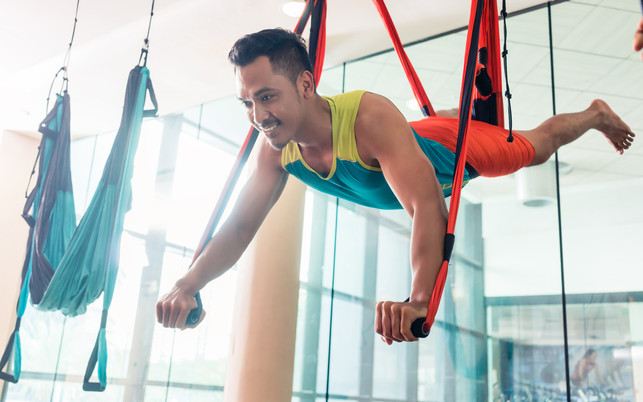Fit handsome man smiling while practicing anti-gravity yoga Für Aerial Yoga brauchst du ein spezielles Tuch.
