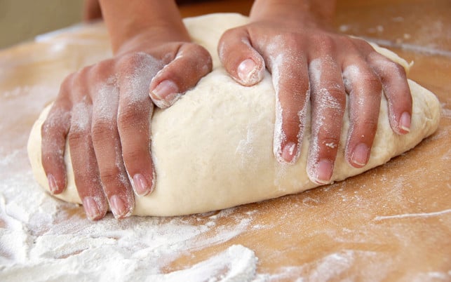 female hands in flour closeup kneading dough on table Es lohnt sich, den Franzbrötchenteig lange zu kneten, damit er geschmeidig wird.