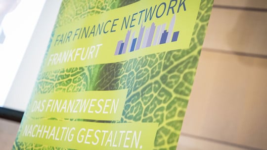 FairFinanceWeek_OSC2729_1920x1080px Grünes Banner mit der Aufschrift „Fair Finance Network Frankfurt“ und „Das Finanzwesen nachhaltig gestalten“ vor einem Hintergrund mit Blattstruktur.