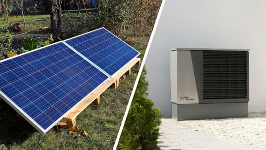 251022-warmepumpe-und balkonkraftwerk-cc0-pb-julianaffeldt_pexels-alpha-innotec Links zwei auf einem Holzgestell montierte Solarpaneele auf einer Wiese, rechts eine graue Wärmepumpe mit schwarzem Lüftungsgitter vor einer weißen Hauswand