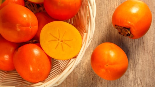 Ripe persimmons in wicker basket on the table, top view Kaki richtig essen