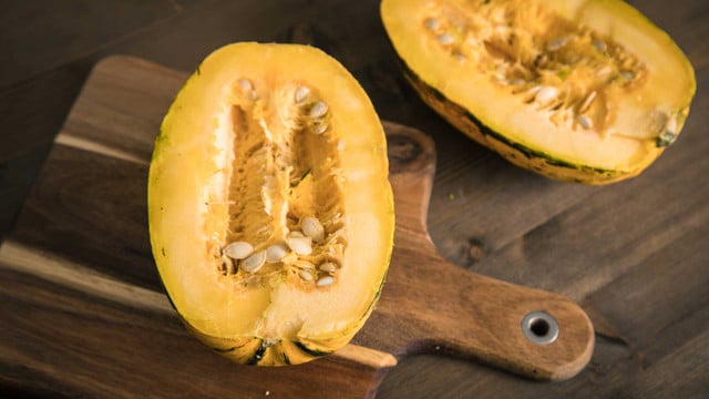 Zwei Hälften eines gelben Kürbisses mit Kernen, liegend auf einem Holzbrett auf einem dunklen Holztisch.