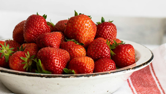Jeden Tag Erdbeeren essen: Das sind die Folgen Eine weiße Schale gefüllt mit frischen, roten Erdbeeren mit grünen Blättern
