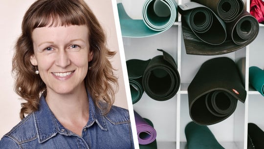 Die richtige Yogamatte für dich finden: Yogalehrerin gibt Tipps Porträt einer lächelnden Frau mit schulterlangen, gewellten braunen Haaren und kurzem Pony, die eine blaue Jeansjacke trägt. Daneben sind mehrere aufgerollte Yogamatten in verschiedenen Farben in einem weißen Regal zu sehen.