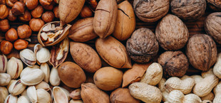 Verschiedene ungeschälte Nüsse, darunter Haselnüsse, Pekannüsse, Walnüsse, Pistazien und Erdnüsse, dicht nebeneinander angeordnet.