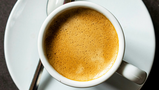 Die beste Tageszeit zum Kaffeetrinken Weiße Tasse mit frisch gebrühtem Espresso, darauf eine feine, goldbraune Crema, auf weißem Unterteller