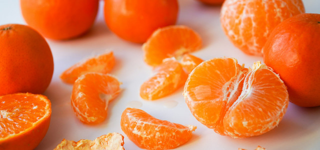 Jeden Tag Mandarinen essen: Das sind die Folgen (Foto: CC0 Public Domain / Unsplash.com – Karolina Kołodziejczak) Mehrere Mandarinen, einige ganz, andere geschält, sowie einzelne Mandarinenstücke und Schalenstücke auf weißem Untergrund.