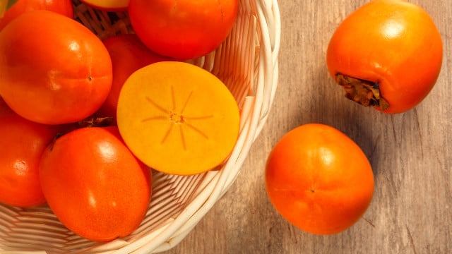Ripe persimmons in wicker basket on the table, top view Kaki richtig essen