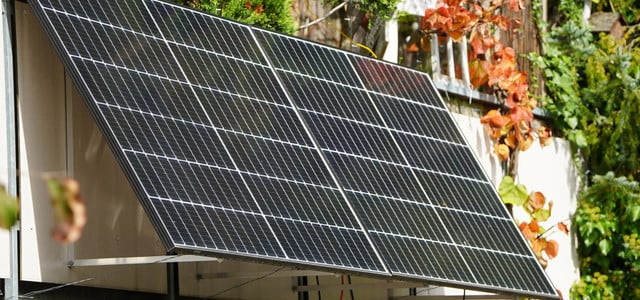 Ist ein Speicher für dein Balkonkraftwerk sinnvoll? So rechnest du es aus (CC0 Public Domain / Pexels – Kindel Media) Zwei Solarpaneele sind an ein Balkongeländer montiert, umgeben von grünen und herbstlich gefärbten Pflanzen.