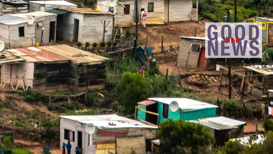 Einfach, aber effektiv: Studie findet kostengünstige Maßnahme gegen Hitzebelastung in Afrika Mehrere einfache Häuser aus Holz und Wellblech in einem ländlichen Gebiet, umgeben von Vegetation und unbefestigten Wegen, mit einigen Menschen im Vordergrund.