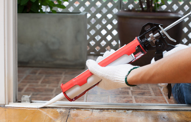Carpenter applies silicone caulk on the wooden floor for sealing waterprof Mit der Kartuschenpresse lassen sich Silikonfugen präzise erneuern.