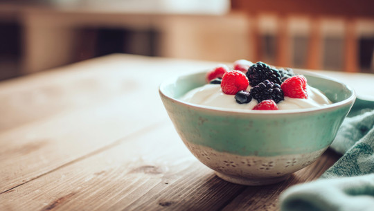 Jeden Tag Skyr essen: Das sind die Folgen Schale mit Skyr, garniert mit frischen Himbeeren, Brombeeren und Heidelbeeren, auf einem Holztisch