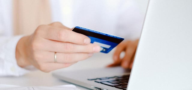 Zum 16. Mal in Folge: Das ist die „Bank des Jahres“ 2025 (Foto: CC0 / Pexels - Anna Shvets) Hand mit silbernem Ring hält eine blaue Kreditkarte vor einem geöffneten silbernen Laptop, auf einem weißen Tisch liegen ein Stift und ein Notizbuch.