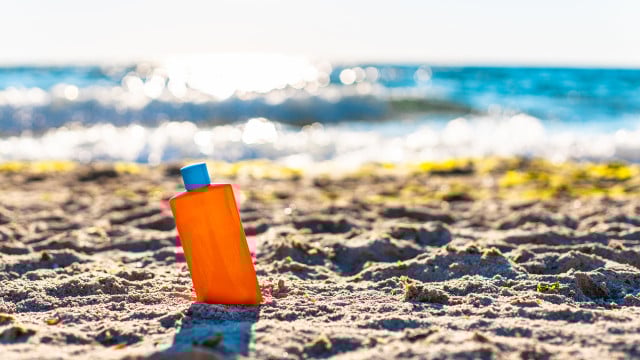Sun protection and skin pigmentation. Orange plastic sunscreen or lotion bottle on the sand near the sea. Sunblocker sind in der EU verboten