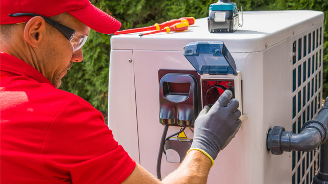 Wärmepumpen-Installation: Smart Meter ist Pflicht Techniker in rotem Hemd, roter Kappe und Schutzbrille arbeitet an einer weißen Wärmepumpe im Freien.