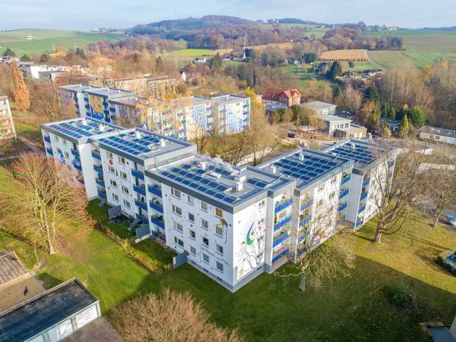 251120-solaranlage-mehrfamilienhaus-meiterstom-gebaedeversorgung-cc0-pb-solarimo Mehrere Wohngebäude mit weißen Fassaden und blauen Balkonen, auf deren Flachdächern zahlreiche Solarpaneele installiert sind.