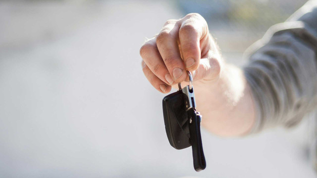 Carsharing: Wann es sich lohnt und wie du dabei Geld sparen kannst Hand, die einen Schlüsselanhänger mit einem Autoschlüssel hält, vor unscharfem Hintergrund.