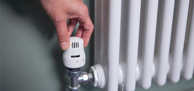 Hand dreht an Heizkörper-Thermostat