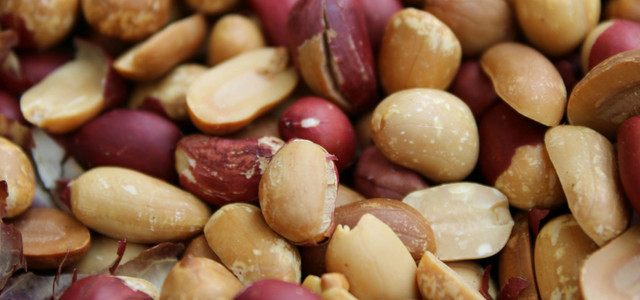 Nahaufnahme von ungeschälten und teilweise geschälten Erdnüssen mit brauner und rötlicher Schale.