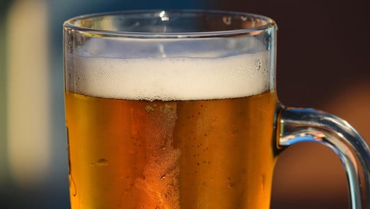 Jeden Abend ein Bier: Das sind die Folgen für Psyche und Körper Ein Glas Bier mit Schaumkrone, das leicht beschlagen ist und in warmem Licht leuchtet.