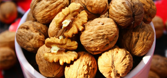 Eine weiße Schale gefüllt mit ganzen Walnüssen in der Schale und zwei aufgebrochenen Walnusshälften, die das Innere zeigen.