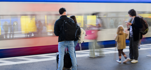 Personen mit Gepäck auf einem Bahnsteig vor einer Bahn