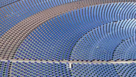 Deutschland hinkt hinterher: Wie China den Markt für grüne Technologie dominiert Luftaufnahme eines großen Solarthermiekraftwerks mit zahlreichen kreisförmig angeordneten, blauen Spiegeln, die das Sonnenlicht bündeln. Die Spiegel sind auf einer sandigen Fläche installiert und reflektieren den Himmel.