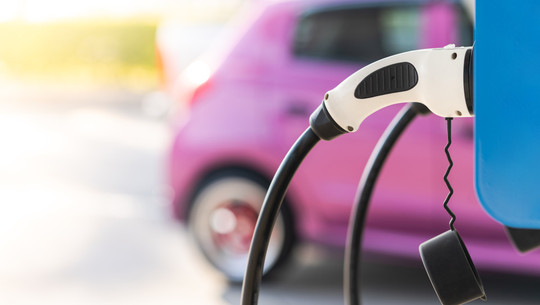 e-auto-ladesaeule-cb-260121 Ladestecker einer Elektroauto-Ladestation mit unscharfem, pinkfarbenem Auto im Hintergrund